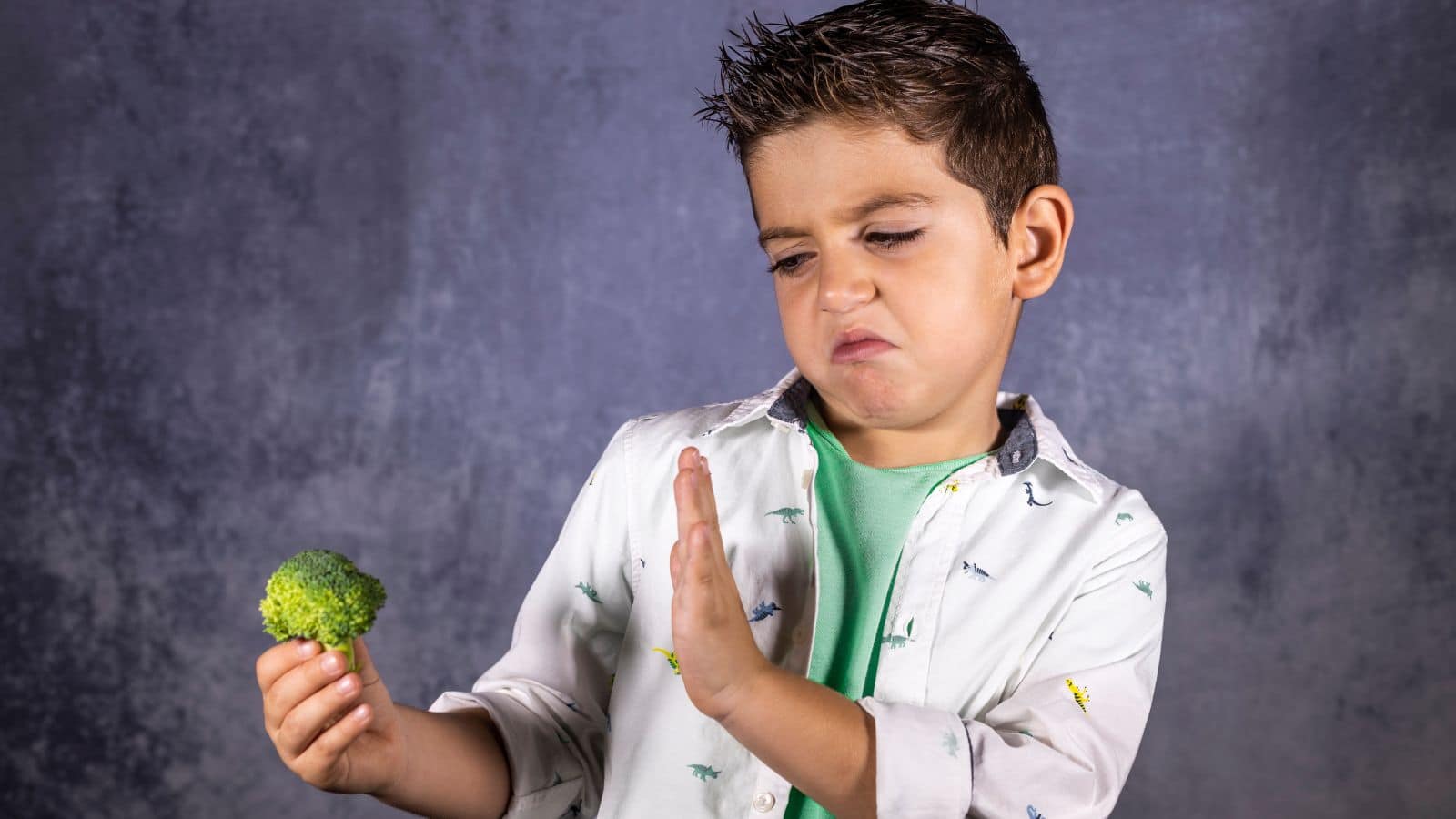 Young boy refusing a stalk of broccoli