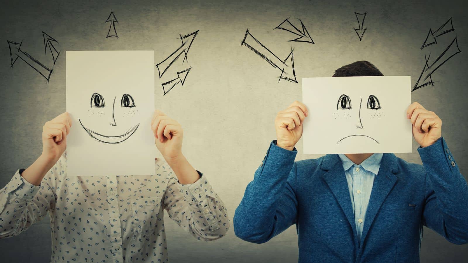Two people holding up sheets of paper in front of their faces - one has a drawing of a smiley face and one is a sad face